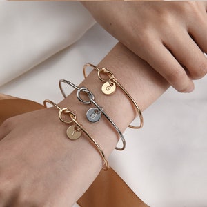 May include: Three gold and silver bracelets with knot details and initial charms. The charms are round and feature the letters G, D, and F.