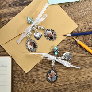 May include: Two silver photo charms with white ribbons and blue beads. The charms feature oval-shaped photos and a heart-shaped charm with the text "You are always in my heart".