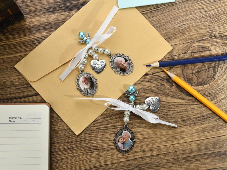 May include: Two silver photo charms with white ribbons and blue beads. The charms feature oval-shaped photos and a heart-shaped charm with the text "You are always in my heart".
