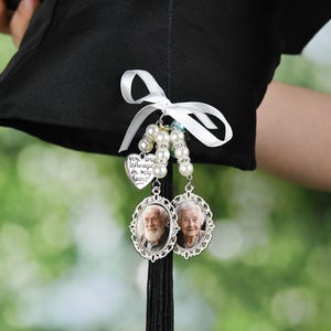 May include: A black graduation cap with a white ribbon and a charm with a heart that says "You are always in my heart" and two oval charms with photos of older people.