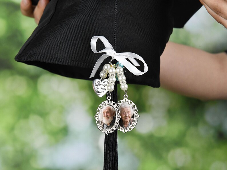 May include: A black graduation cap with a white ribbon and a charm with a heart that says "You are always in my heart" and two oval charms with photos of older people.