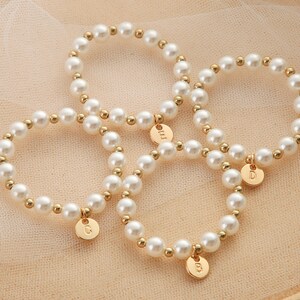 May include: Three gold pearl bracelets with initial charms. The charms are gold and have the letters C, D, and M on them.