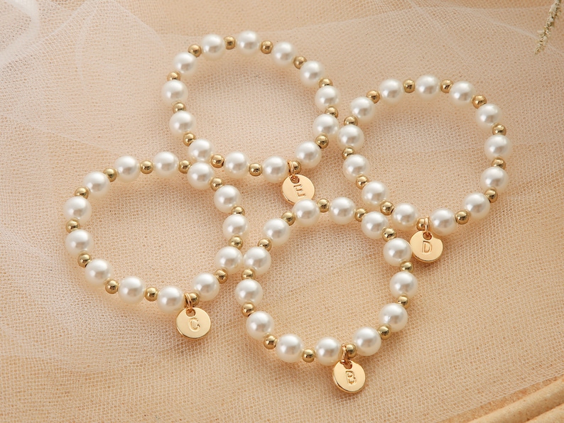May include: Three gold pearl bracelets with initial charms. The charms are gold and have the letters C, D, and M on them.