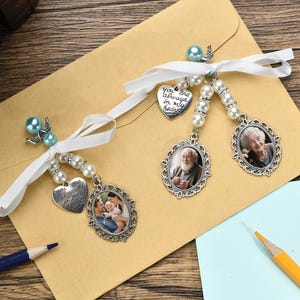 May include: Two white satin ribbons with pearl beads and silver charms. The charms include a heart with the text "You are always in my heart", a photo frame with a man in it, a photo frame with a woman in it, and a photo frame with a couple and a child in it.
