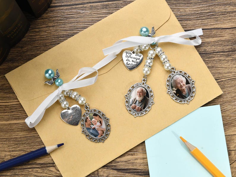 May include: Two white satin ribbons with pearl beads and silver charms. The charms include a heart with the text "You are always in my heart", a photo frame with a man in it, a photo frame with a woman in it, and a photo frame with a couple and a child in it.
