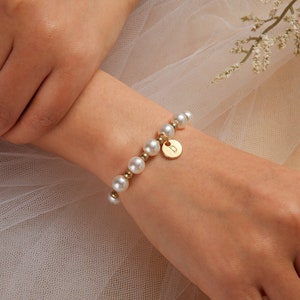 May include: A gold bracelet with a pearl and gold bead design. The bracelet has a small gold charm with a letter 'D' on it.