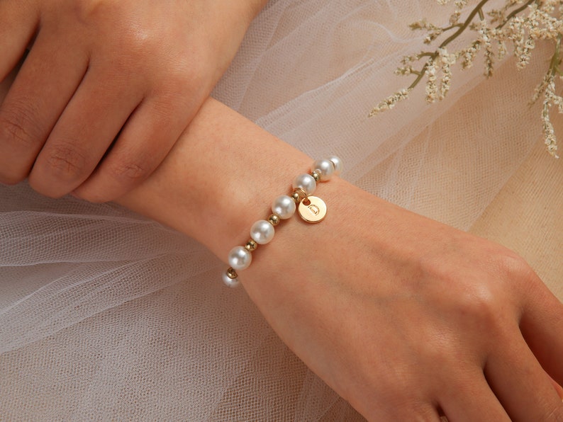 May include: A gold bracelet with a pearl and gold bead design. The bracelet has a small gold charm with a letter 'D' on it.