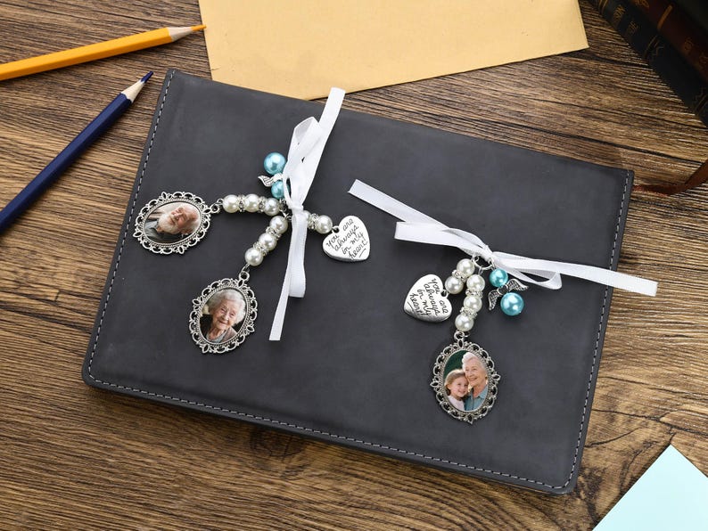 May include: Two silver memorial car charms with white ribbons and pearl beads. One charm features a heart with the text "You are always in my heart". The other charm features a photo of two people.