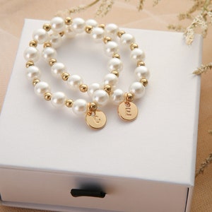 May include: Two pearl bracelets with gold accents and personalized charms. The charms are round and have the letters "G" and "M" engraved on them.