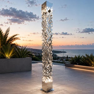 May include: A tall, vertical floor lamp featuring a reflective, polished chrome finish with an intricate, open-work geometric lattice structure. The design consists of stacked, angular metal segments that create a complex, light-diffusing pattern.