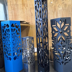 May include: A selection of decorative metal lanterns in various colours and designs. The lanterns are square or rectangular, with intricate cut-out patterns. Colours include blue, black, and silver. The tallest lantern is approximately 91 cm tall.