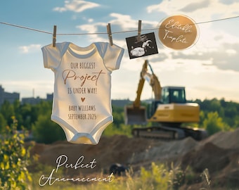 以下が含まれることがあります： 白いロンパースに「Our Biggest Project Is Under Way!」と「Baby Williams September 2025」という茶色の文字が書かれています。ロンパースは洗濯ロープにかけられており、背景には建設車両があります。
