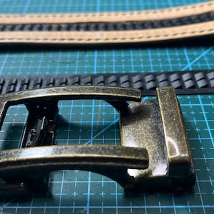 May include: A gold-toned metal belt buckle with a rectangular frame and a curved, smooth top. The buckle has a worn, antique finish.