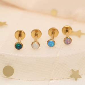 Può includere: Quattro orecchini dorati con retro piatto e pietre preziose di opale. I colori dell'opale includono verde, bianco, blu e rosa. Gli orecchini hanno un design a perno e disco piatto.