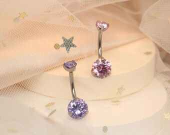 May include: Two belly button rings with clear posts and jeweled tops. One ring has a light purple gem and the other has a light pink gem.