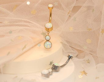 May include: Two belly button rings with white opal stones. The ring on the left has a dangling charm with two more opal stones. The ring on the right has a single opal stone.