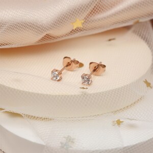 May include: A pair of rose gold stud earrings with small, clear cubic zirconia stones.