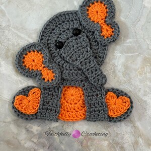 May include: A handmade crochet elephant in gray and orange. The elephant has large ears with orange centers, black eyes, and orange accents on its feet and belly. The text "Faithfully Crocheting" is at the bottom.