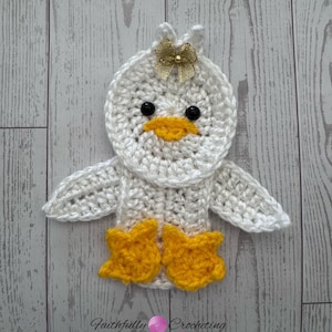 May include: A handmade white crochet duckling with a gold bow, black eyes, and a yellow beak and feet. The duckling has outstretched wings. The text "Faithfully Crocheting" is at the bottom.