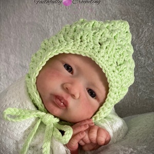May include: A light green crocheted baby bonnet with a matching tie. The bonnet has a simple stitch pattern and is designed to fit a newborn baby.