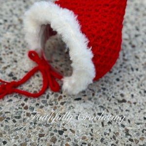 May include: A handmade red crocheted Santa hat with a white faux fur trim. The hat has a pointed top and a red tie. The text "Faithfully Crocheting" is visible on the surface.
