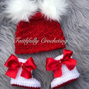 May include: A red crocheted baby hat with two white fluffy pom-poms and matching white crocheted baby booties with red satin bows. The text "Faithfully Crocheting" is visible on the hat.