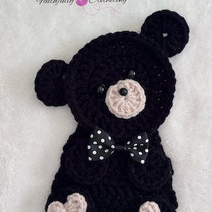 May include: A black crocheted bear applique featuring a light beige muzzle, two black bead eyes, and a black bow tie with white polka dots. The bear has two round ears and two light beige heart-shaped patches on its feet. Text reads Faithfully Crocheting.