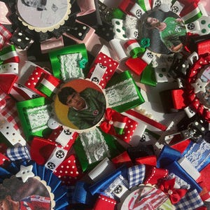 May include: A collection of handmade ribbon rosettes featuring circular photo inserts of soccer players. The rosettes are crafted from various patterned ribbons in red, white, green, black, and blue, accented with lace, small buttons, and metal clips.