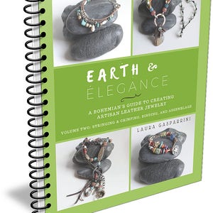 Pode incluir: Um livro verde intitulado "Earth & Elegance: A Bohemian's Guide to Creating Artisan Leather Jewelry, Volume Two: Stringing & Crimping, Binding, and Assemblage" de Laura Gasparrini. A capa apresenta fotos de joias artesanais sobre pedras.