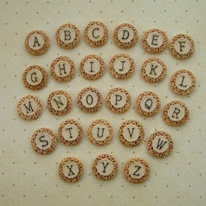 May include: A set of 26 round ceramic tiles with a decorative border and a letter of the alphabet printed in black on each tile.