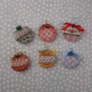 May include: Six miniature circular ornaments featuring varied patterns and colors. Each piece includes a small hanging loop at the top, with some adorned with tiny bows or decorative accents in red, gold, silver, and blue ribbons.