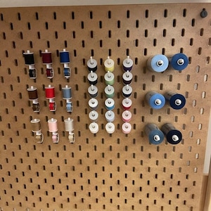 May include: A pegboard with various spools of thread in different colours, including red, blue, green, and white. The spools are organised in rows and columns on the pegboard.