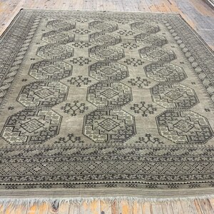 Puede incluir: Una alfombra grande y rectangular con un diseño persa tradicional. La alfombra es de color beige claro con un patrón marrón oscuro. El patrón presenta intrincadas formas geométricas y motivos florales. La alfombra tiene un borde con flecos.