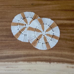 Può includere: Due sottobicchieri rotondi in macramé bianco e marrone con frange. I sottobicchieri hanno un motivo geometrico.