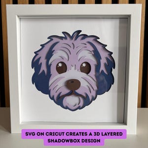 Puede incluir: Una pieza de arte en papel en capas de la cara de un perro en un marco blanco. El perro tiene pelo morado claro y azul oscuro, ojos marrones y una nariz marrón. El texto en la parte inferior dice "SVG ON CRICUT CREATES A 3D LAYERED SHADOWBOX DESIGN."
