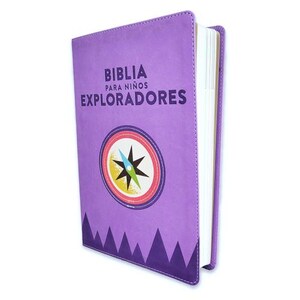 May include: A purple Bible for children with the text "BIBLIA PARA NIÑOS EXPLORADORES". The cover features a compass design and a mountain range at the bottom. The book has a white spine and pages.