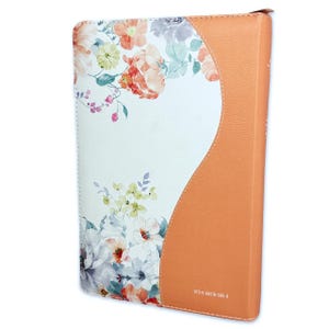 May include: A white and orange leather-bound journal with a floral design. The journal has a curved spine and a floral pattern on the front cover. The back cover is solid orange leather. The text "978-8-85516-085-0" is printed on the back cover.