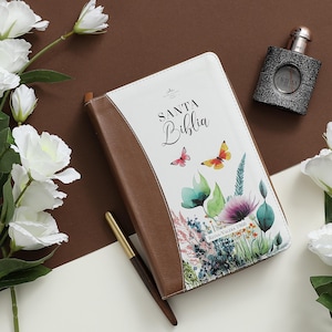 Puede incluir: Un diario encuadernado en cuero marr&oacute;n con una cubierta blanca que presenta un dise&ntilde;o floral y el texto "Santa Biblia Reina Valera 1960".