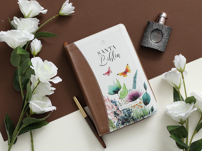 Puede incluir: Un diario encuadernado en cuero marr&oacute;n con una cubierta blanca que presenta un dise&ntilde;o floral y el texto "Santa Biblia Reina Valera 1960".
