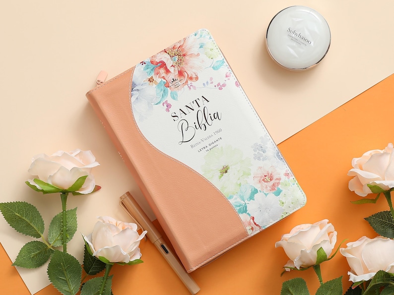 May include: A peach-colored leather-bound journal with a floral design on the cover. The cover reads "SANTA Biblia" with the text "Reina Valera 1960" and "Letra Gigante" underneath.