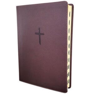 May include: A dark plum-colored hardcover book with a textured, leather-like finish. A simple, dark cross is embossed in the center of the front cover. The page edges are gilded in gold, and the book features thumb index tabs along the side.
