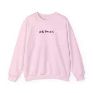 May include: A light pink sweatshirt with the text "code blooded" in a dark brown font across the chest. The sweatshirt has a crew neck and long sleeves, and is made of a soft material.