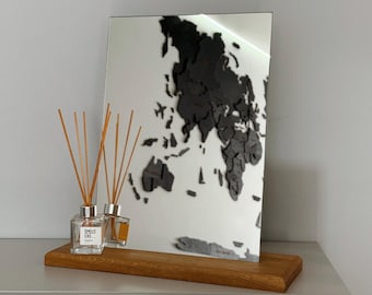 May include: A wooden stand with a mirror reflecting a black world map on the wall. Two glass bottles with wooden sticks are on the stand. The bottles are labelled "Smells Like... Vanilla".