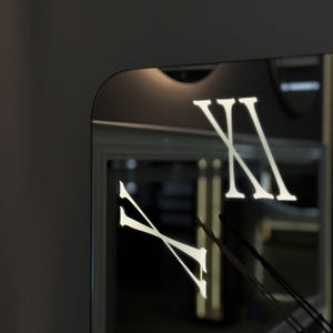 May include: A square wall clock with a black frame and a mirrored face. The clock features white Roman numerals and black clock hands. The design is modern and minimalist.