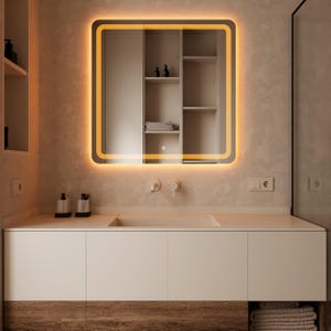 Puede incluir: Un moderno mueble de baño con un espejo rectangular con un borde naranja iluminado. El espejo está montado sobre un mueble blanco con una base de madera. El baño tiene una paleta de colores neutros.