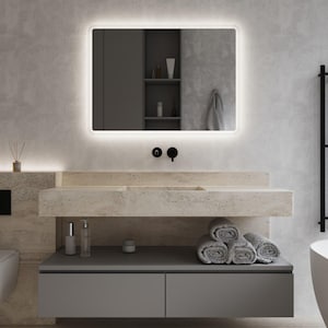Puede incluir: Un moderno mueble de baño con un espejo rectangular con borde luminoso. El mueble tiene una encimera de piedra con lavabo integrado, armarios grises y toallas grises enrolladas. También se ven grifos negros y un inodoro mural.