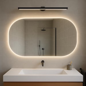 Könnte beinhalten: Ein ovaler, beleuchteter Badezimmerspiegel mit warmem, leuchtendem Rand. Der Spiegel befindet sich über einer weißen Arbeitsplatte mit einem eingebauten Waschbecken. Über dem Spiegel befindet sich eine schwarze Leuchte und ein Zahnbürstenhalter auf der Theke.