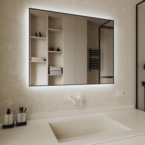 Può includere: Un lavabo da bagno bianco con un piano di lavoro bianco e uno specchio rettangolare grande con cornice nera e una luce bianca attorno al bordo. Lo specchio riflette un bagno bianco con una mensola e un portasciugamani.
