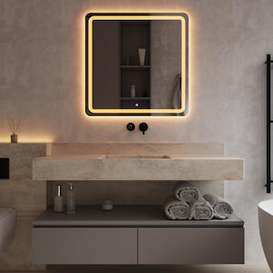 Peut inclure: Scène de salle de bain moderne avec un miroir carré bordé de lumière jaune. En dessous, un plan de travail en pierre avec un lavabo intégré, un meuble gris et des serviettes roulées. Les murs sont de couleur neutre.