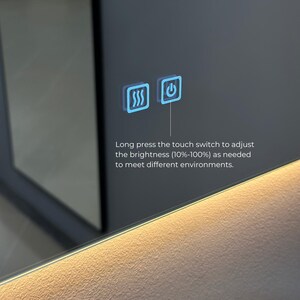 May include: A close-up of a smart mirror with a touch-sensitive control panel. The panel has two icons: a wavy line representing the defogger function and a power button. The text below the icons reads: "Long press the touch switch to adjust the brightness (10%-100%) as needed to meet different environments."